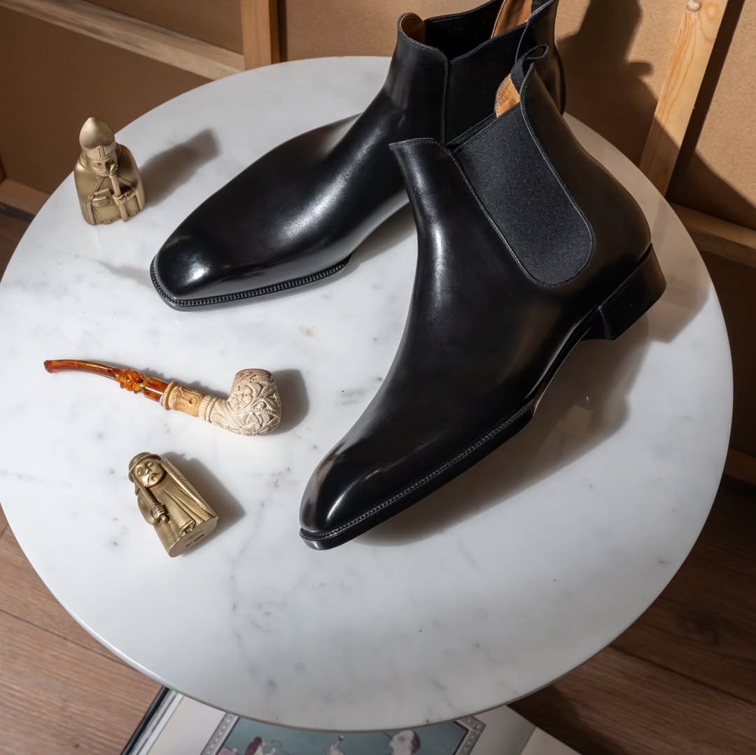 Black leather Chelsea boots on a marble surface with decorative items.